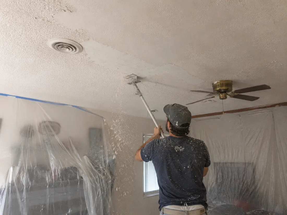 Popcorn ceiling texture being scraped from a ceiling